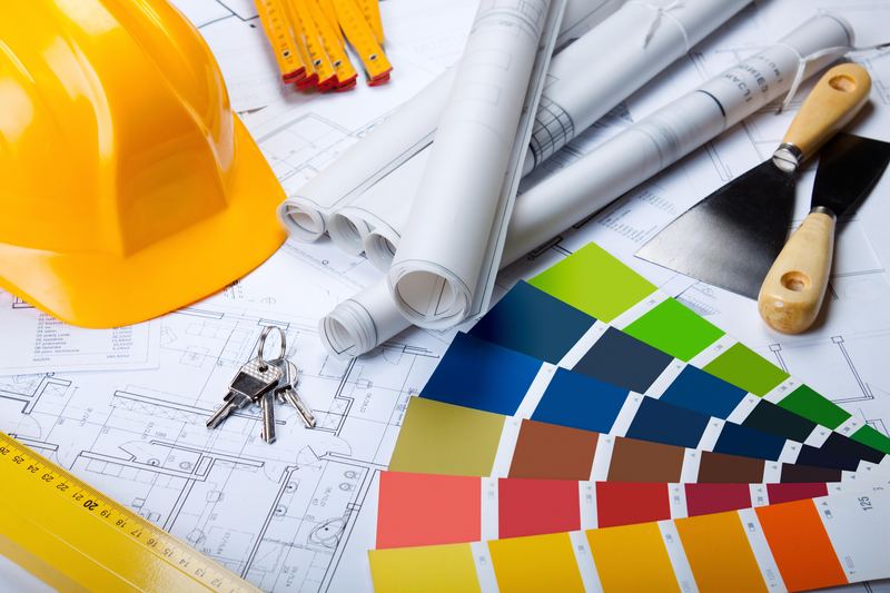 Yellow hard hat, rolled construction drawings, a set of keys and a fanned-out book of finish color samples on printed floor plans