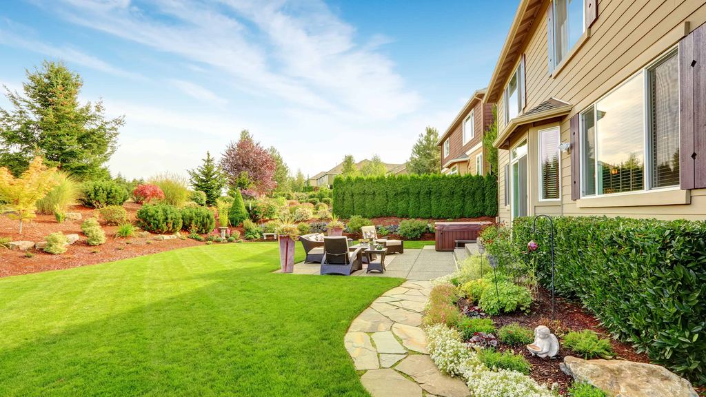 Backyard stone patio with seating beside a freshly mown lawn and mulched beds of shrubs and flowers
